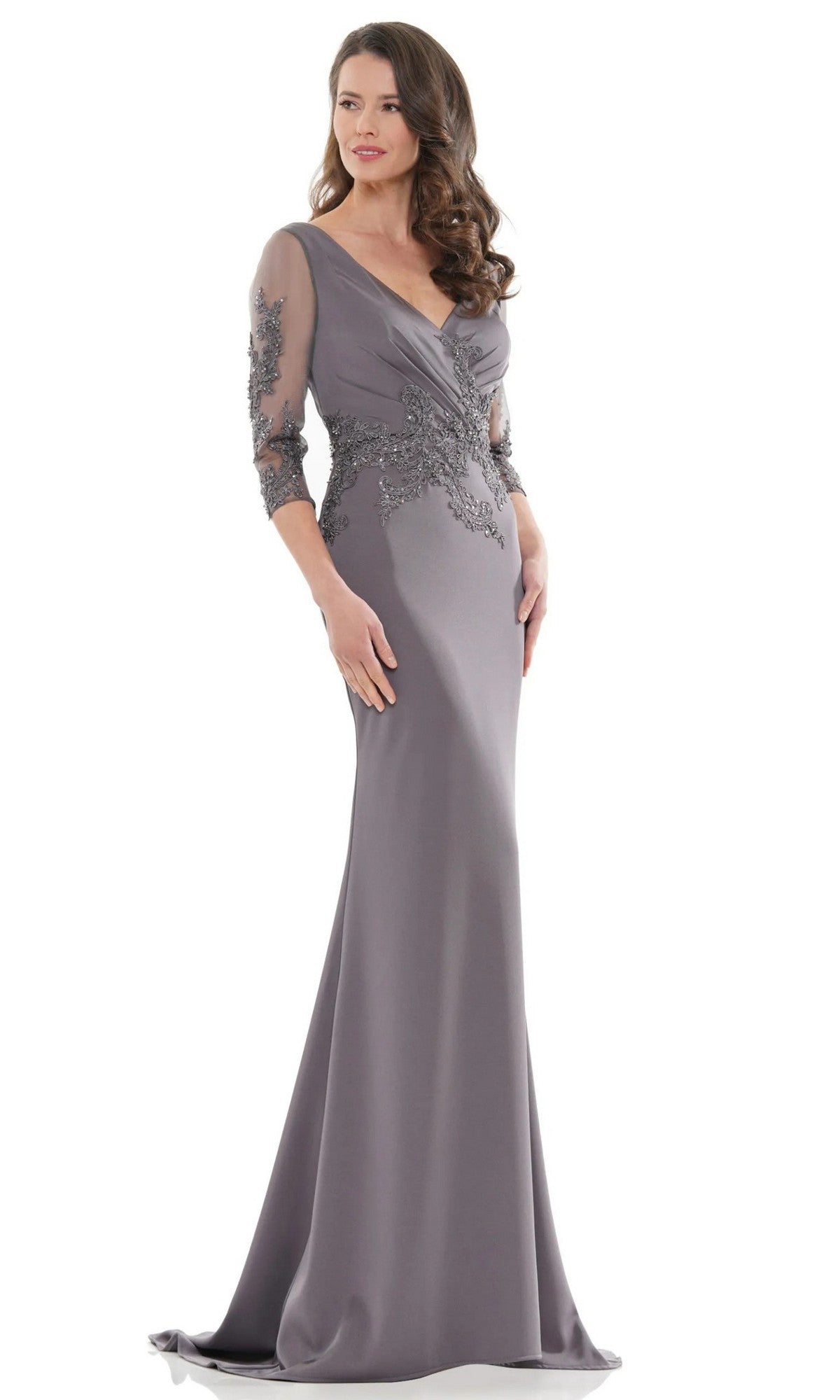A woman stands against a white background wearing the Marsoni MV1145 long formal dress in charcoal, featuring sheer embroidered sleeves and beaded embellishments on the fitted bodice.